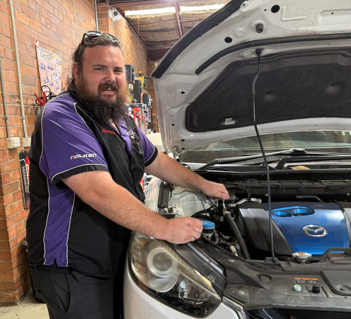 Mechanic smiling beside a car with the hood open in a garage — AutoHop Lambton in Lambton, NSW