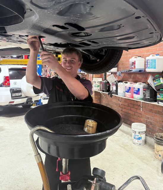Mechanic draining oil from a car on a lift into a black oil pan in a garage — AutoHop Lambton in Lambton, NSW