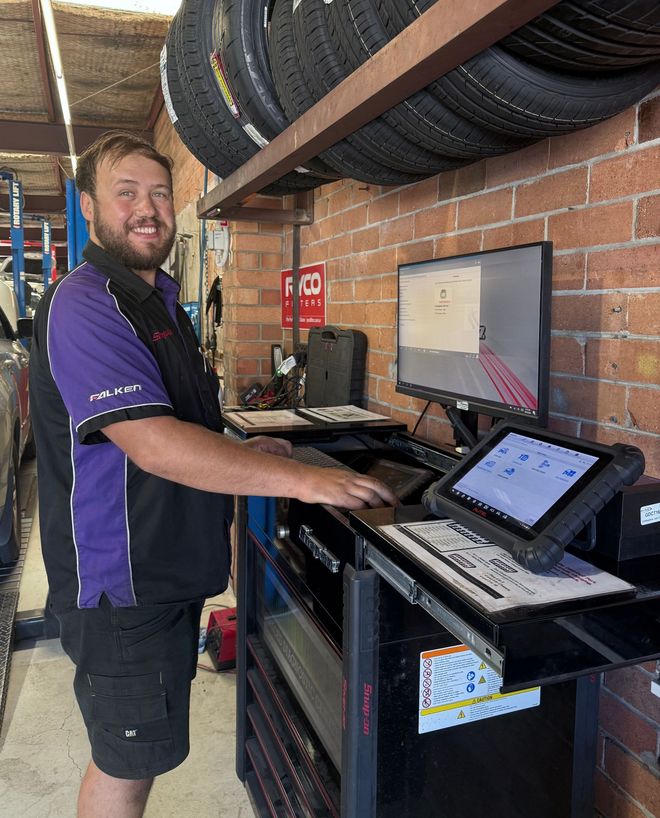 Person standing at a workbench with a laptop in a workshop or warehouse aisle — AutoHop Lambton in Lambton, NSW