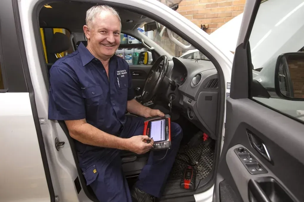Mechanic Smiling While Sitting in a Car Doorway — AutoHop Lambton in Lambton, NSW