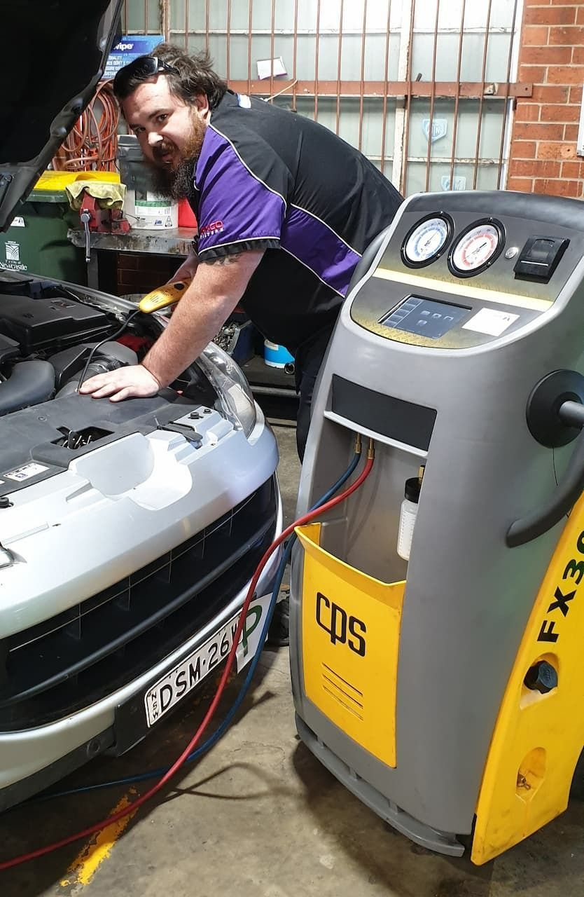 A Mechanic Working on A Car Next to An A/C Service Machine in A Garage Setting — AutoHop Lambton in Lambton, NSW