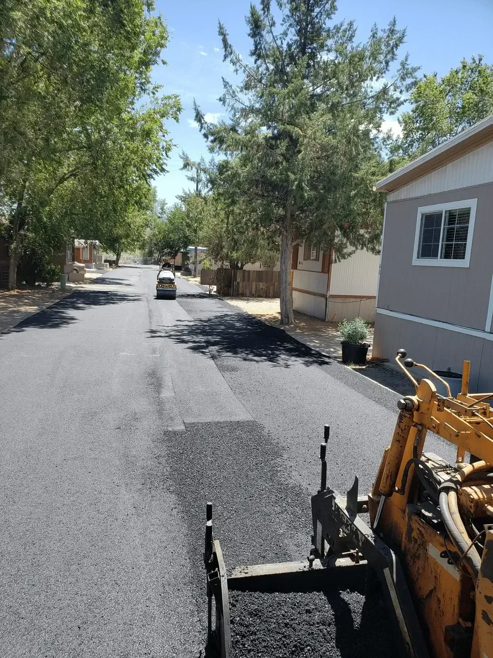 A yellow machine is laying asphalt on the side of a road