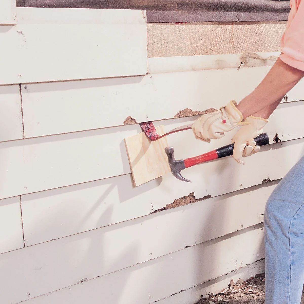 Person hammering siding on a house, using a wooden block to protect the surface.