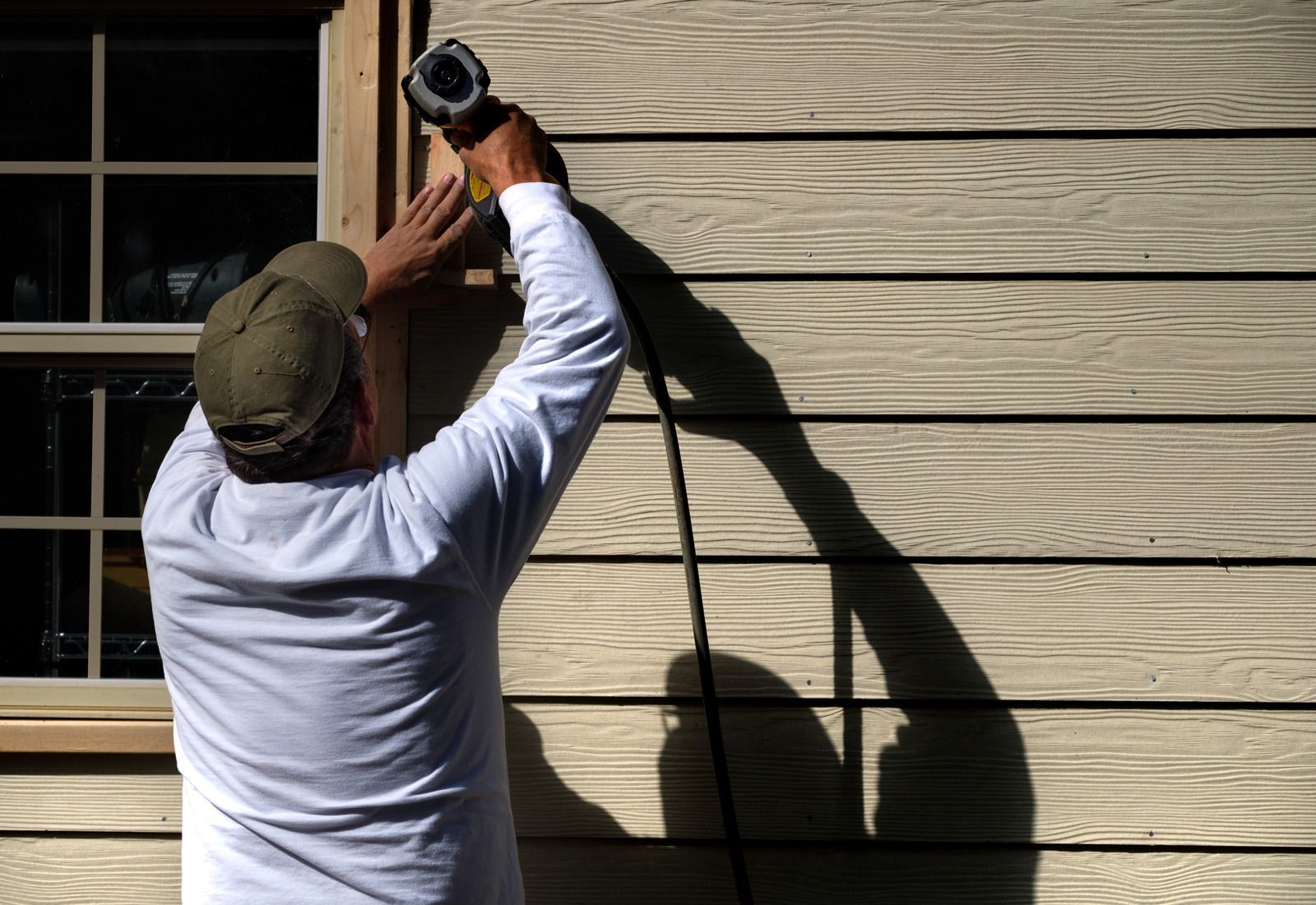 A man is using a drill to fix a window on a house.