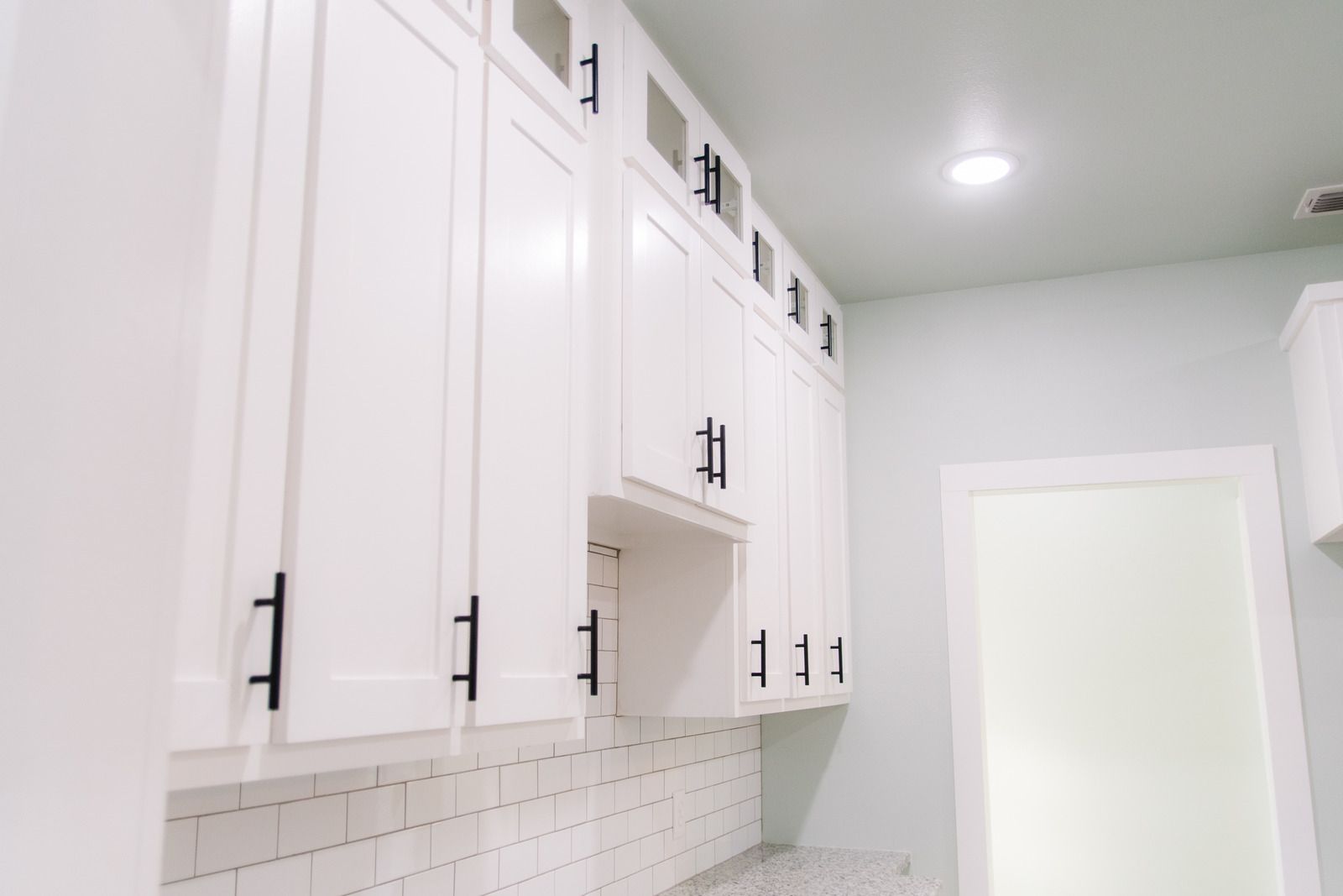 White kitchen cabinets with black hardware against a light-colored tiled backsplash and a light-green wall.