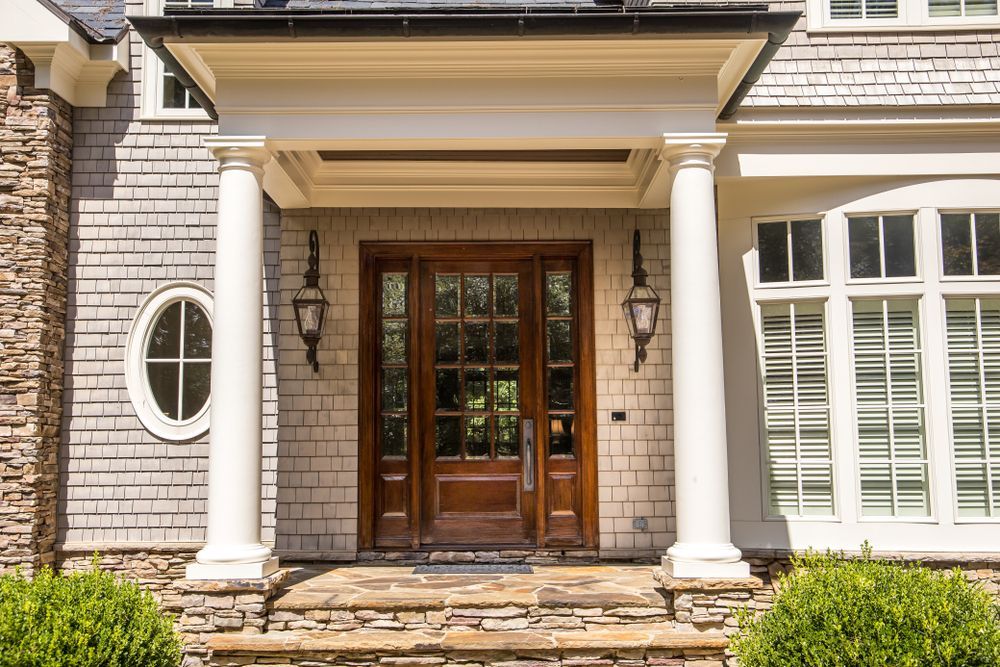 Wooden front door with sidelights, under a white portico supported by columns. Stone steps and cedar shake siding.