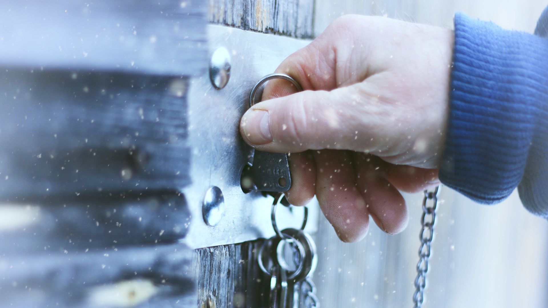 A hand uses a key to lock a door in the snow.