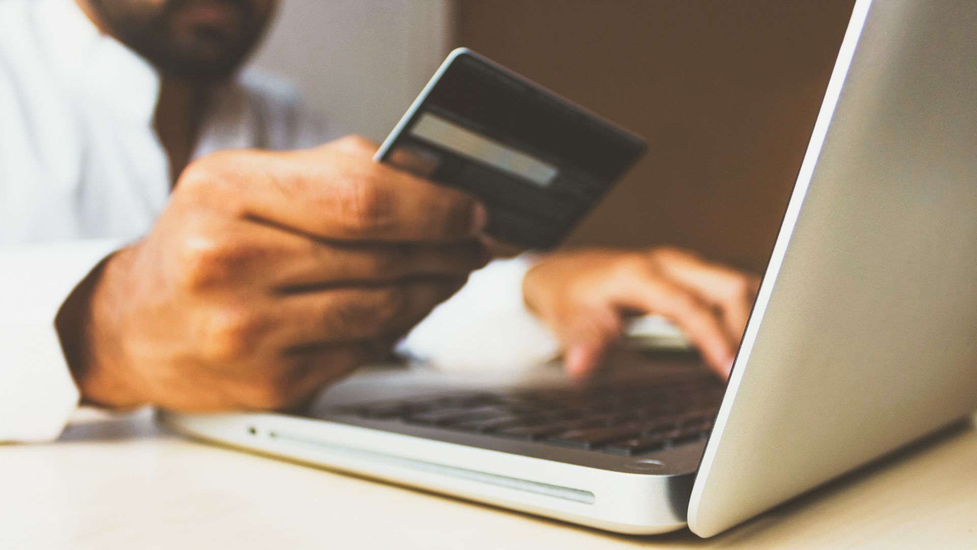 A person holding a credit card and typing on a computer.