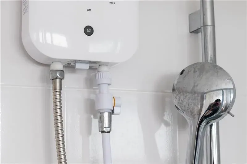 White water heater mounted on a white tiled wall, with silver showerhead and plumbing.