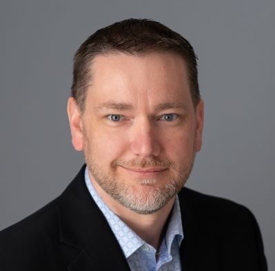 A man with a beard is wearing a suit and smiling for the camera.