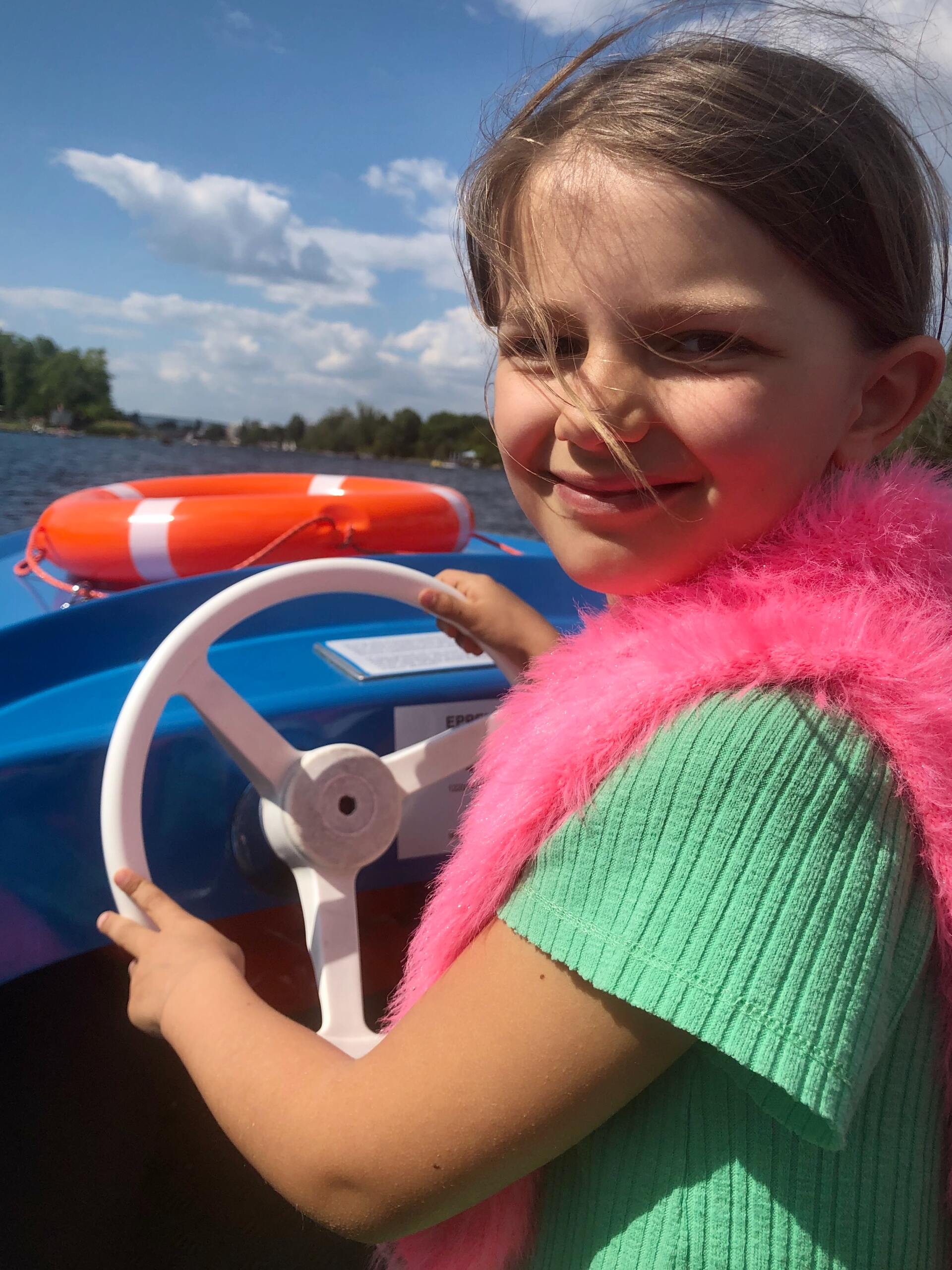 A little girl is holding a steering wheel on a boat.