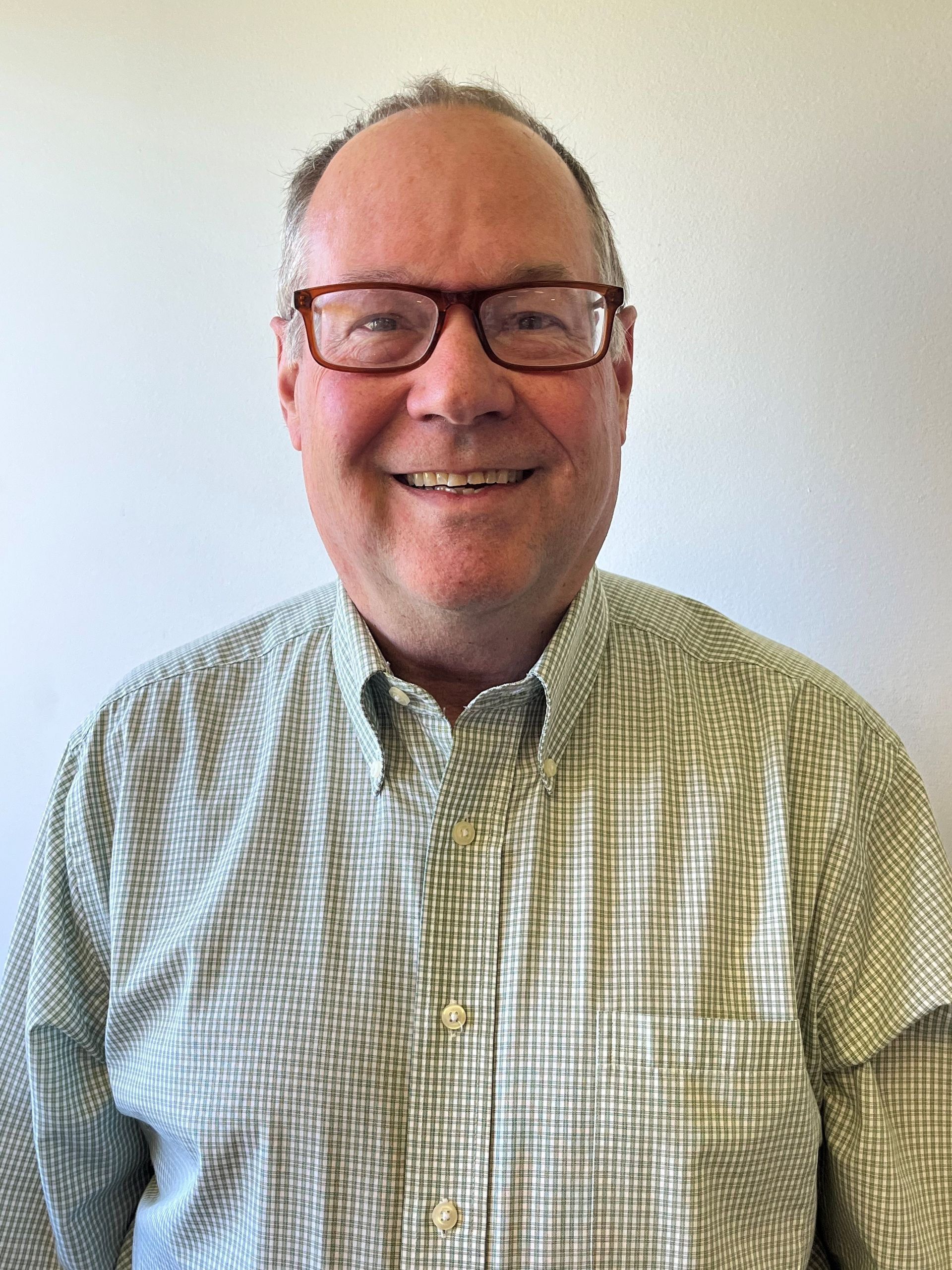 A man wearing glasses and a plaid shirt is smiling for the camera.