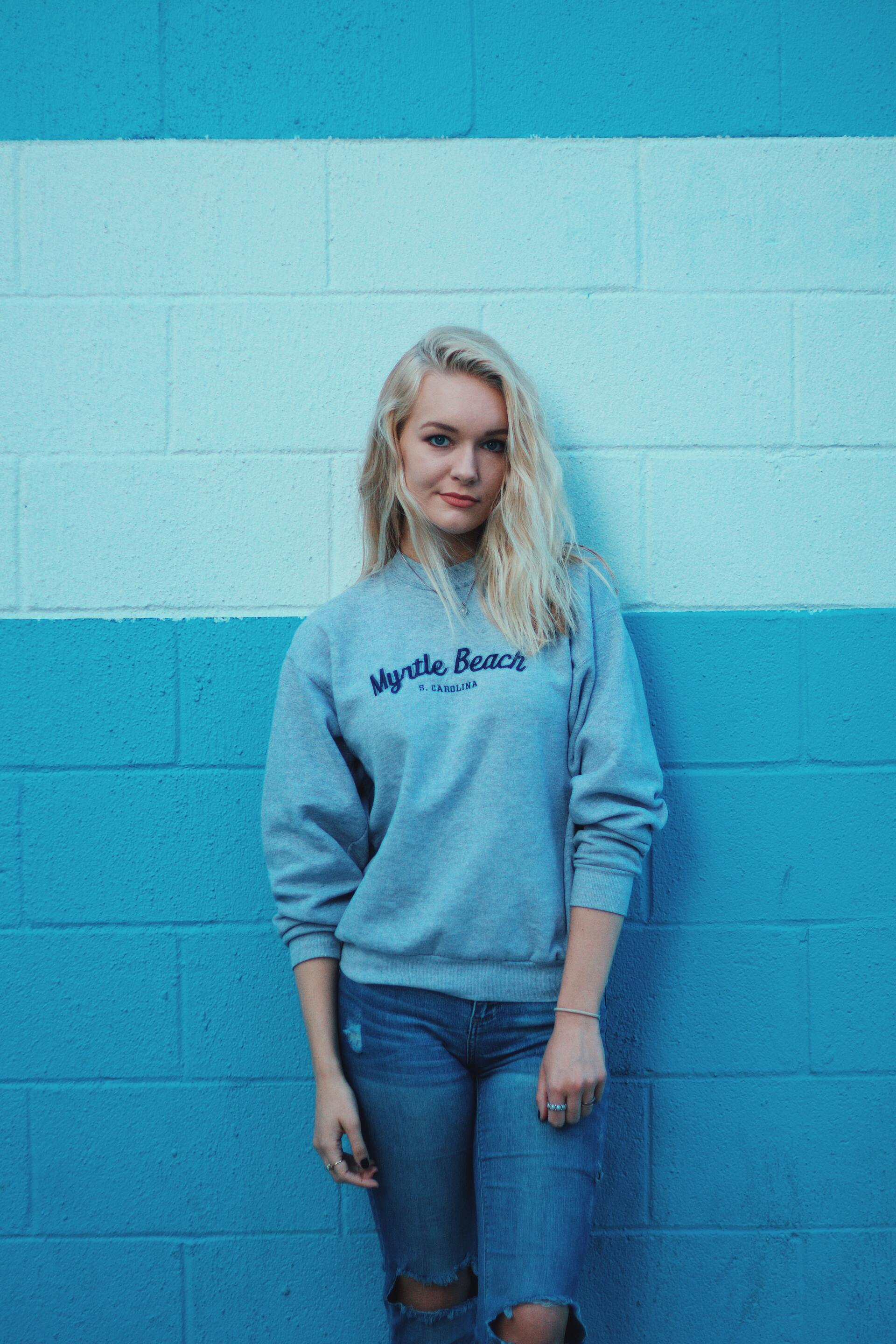 A woman is standing in front of a blue and white brick wall.