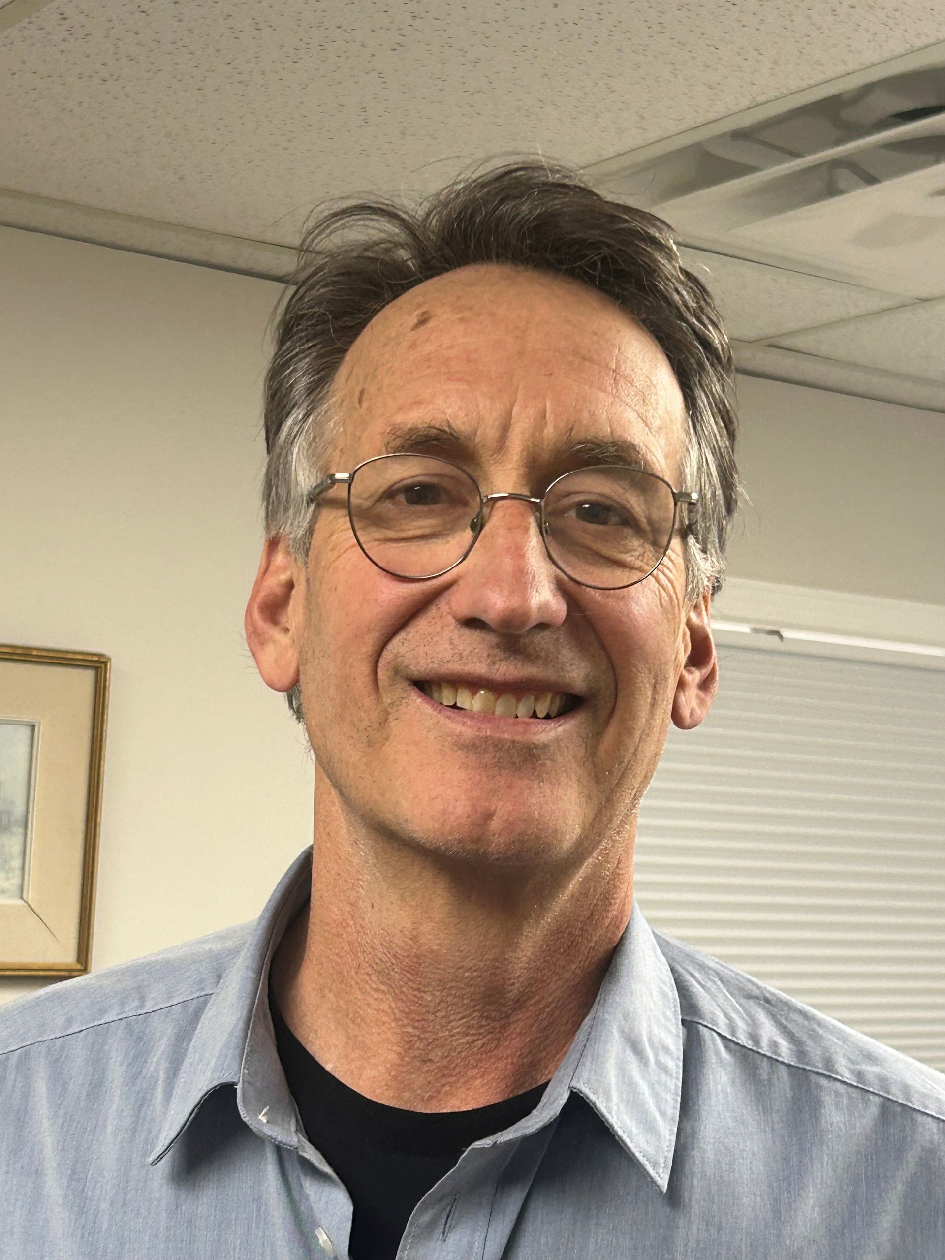 A man wearing glasses and a blue shirt is smiling for the camera.
