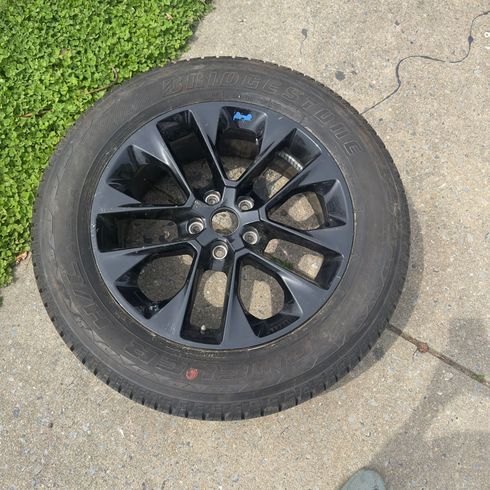Black alloy car wheel with tire lying on a concrete driveway beside grass