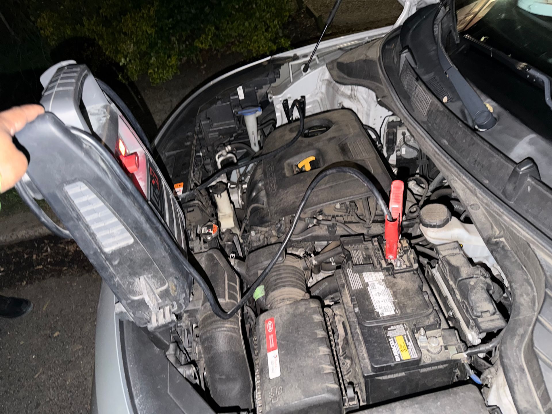 A roadside assistance technician in a high-visibility jacket jump-starts a car battery on a residential street,