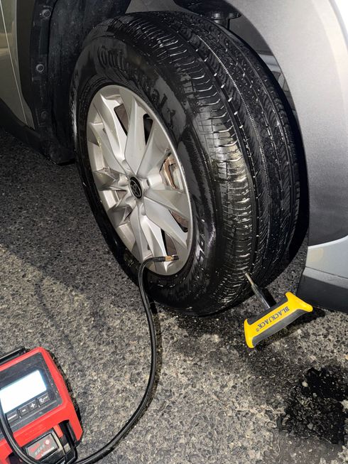 Flat tire on a car at night, with a portable air compressor and a yellow wheel chock beside it.