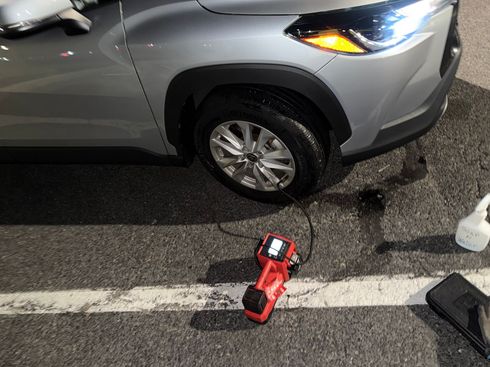 Gray SUV with front wheel damage and a red cordless tool on the pavement beside it