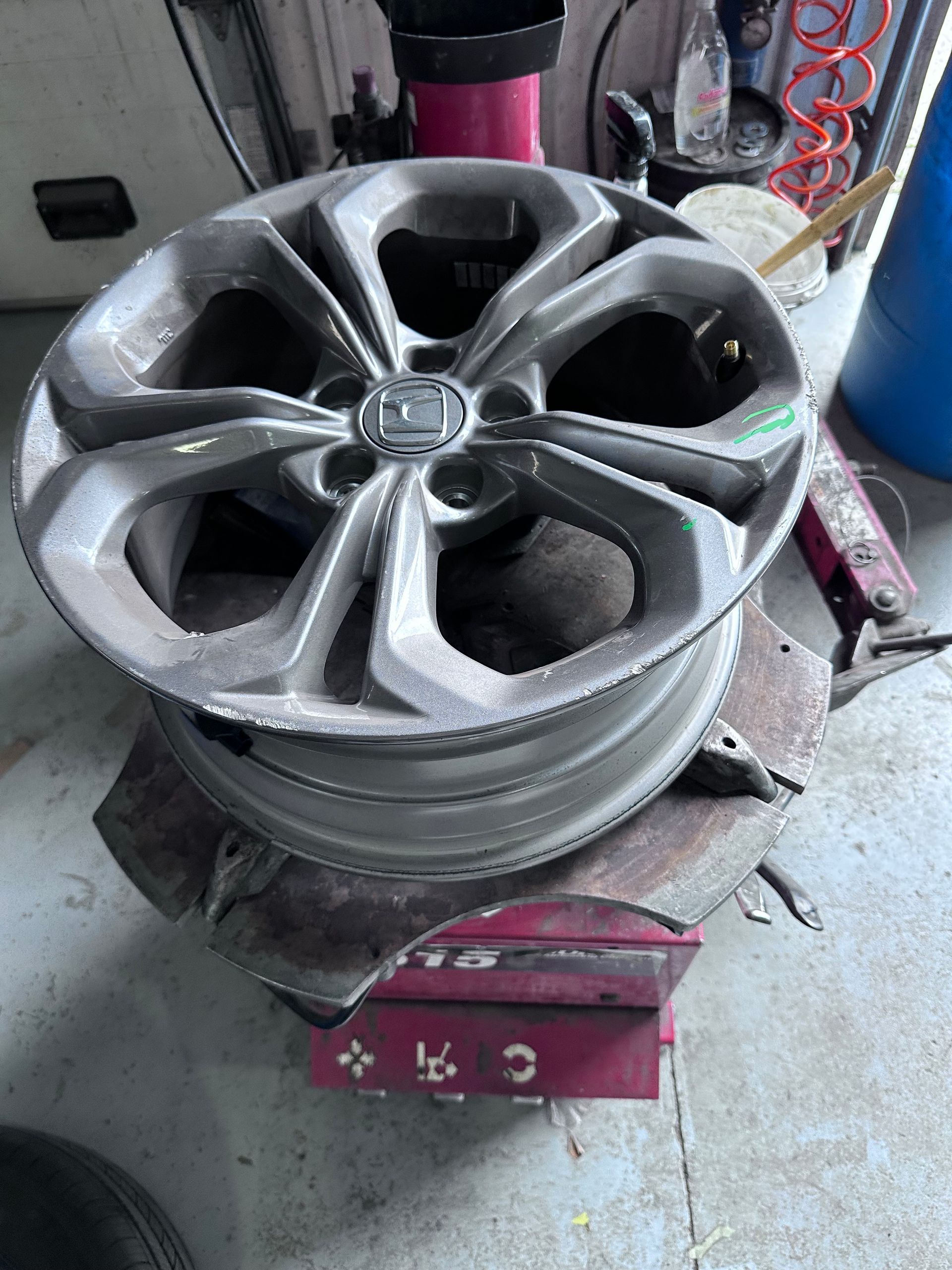 Silver alloy wheel rim on a tire-changing machine in a workshop with pink and blue tools nearby