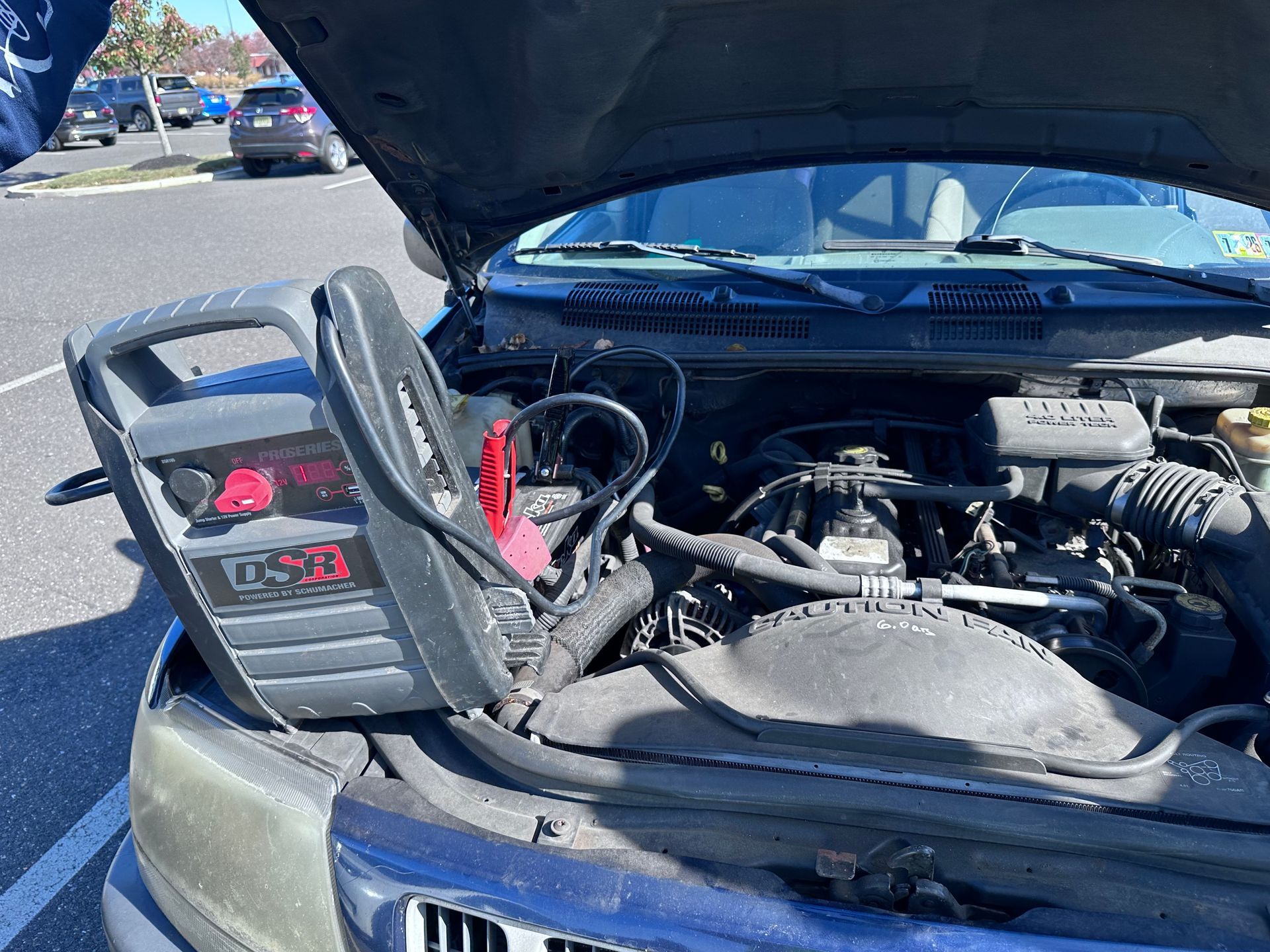 A roadside assistance technician in a high-visibility jacket jump-starts a car battery on a residential street, 