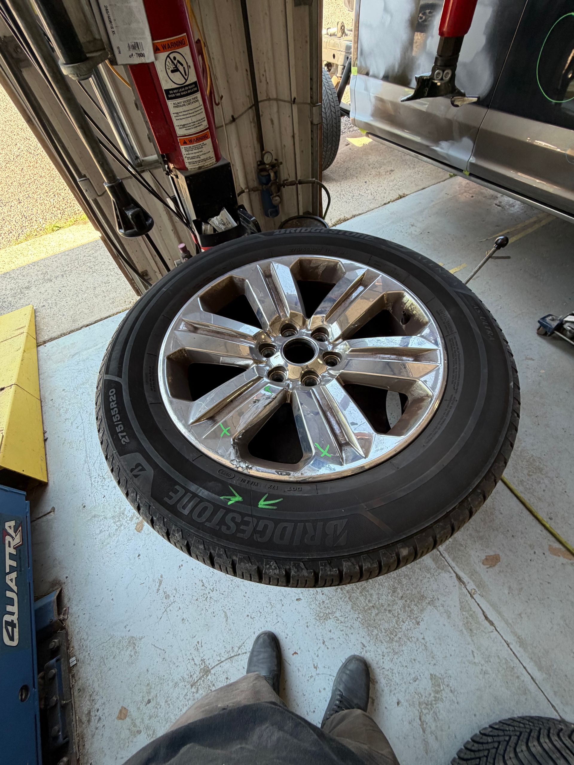 Mechanic kneeling by a silver SUV, tightening a tire lug nut in a suburban driveway.
