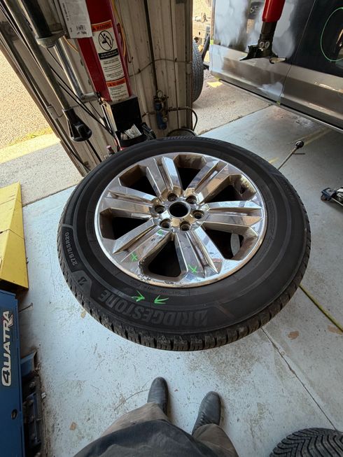 Car tire with chrome rim on a garage floor beside a vehicle lift, viewed from above