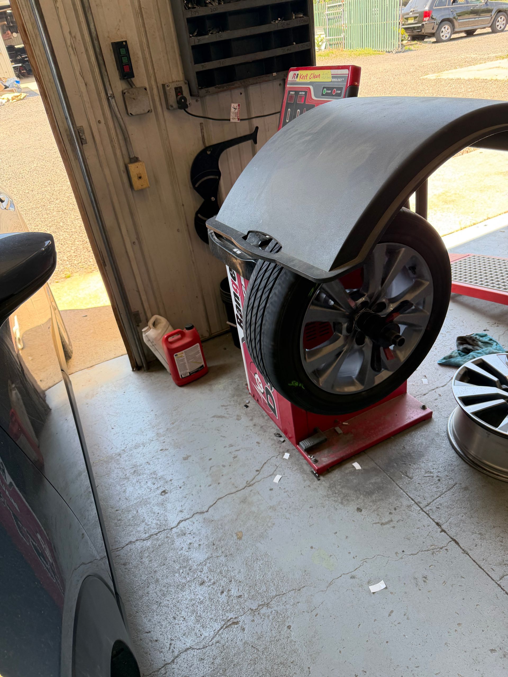 Mechanic kneeling beside a gray car, tightening a lug nut with a tire on the ground.