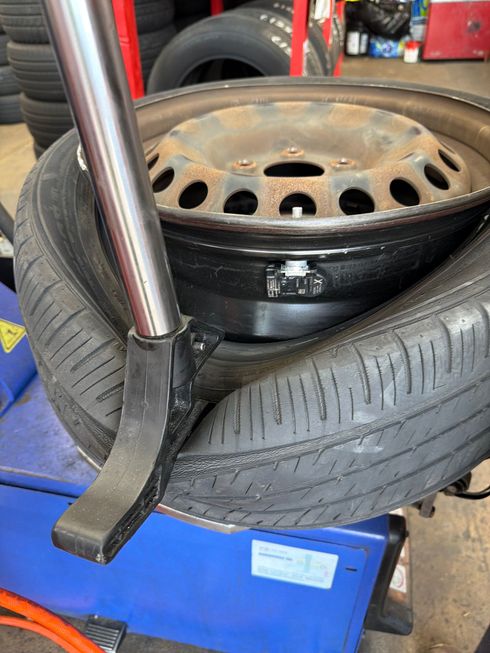 Car wheel and tire on a blue tire-changing machine in a garage, with a chrome pry bar nearby