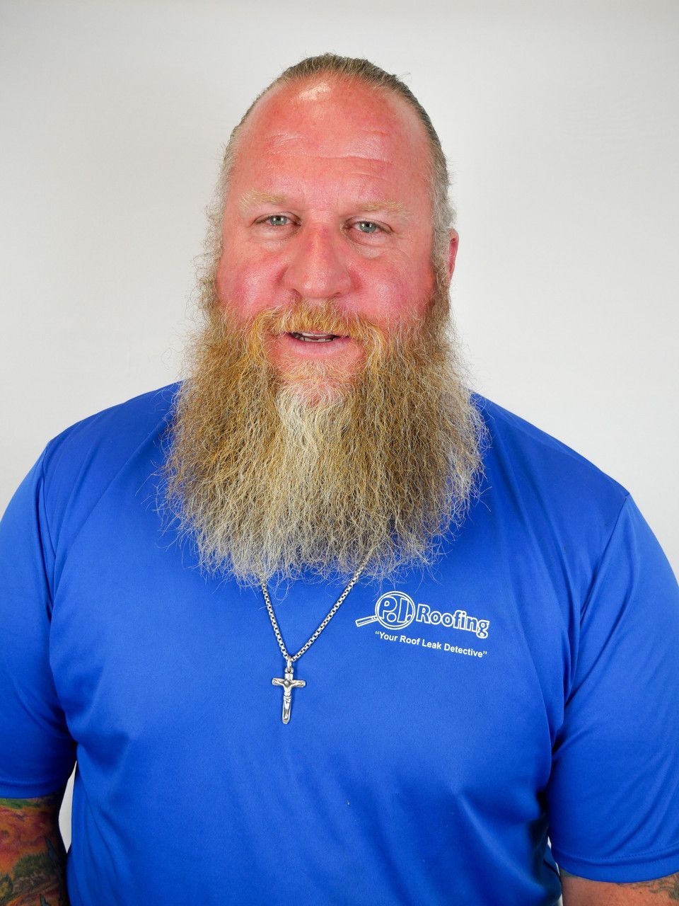 A man with a beard wearing a blue shirt and a cross necklace