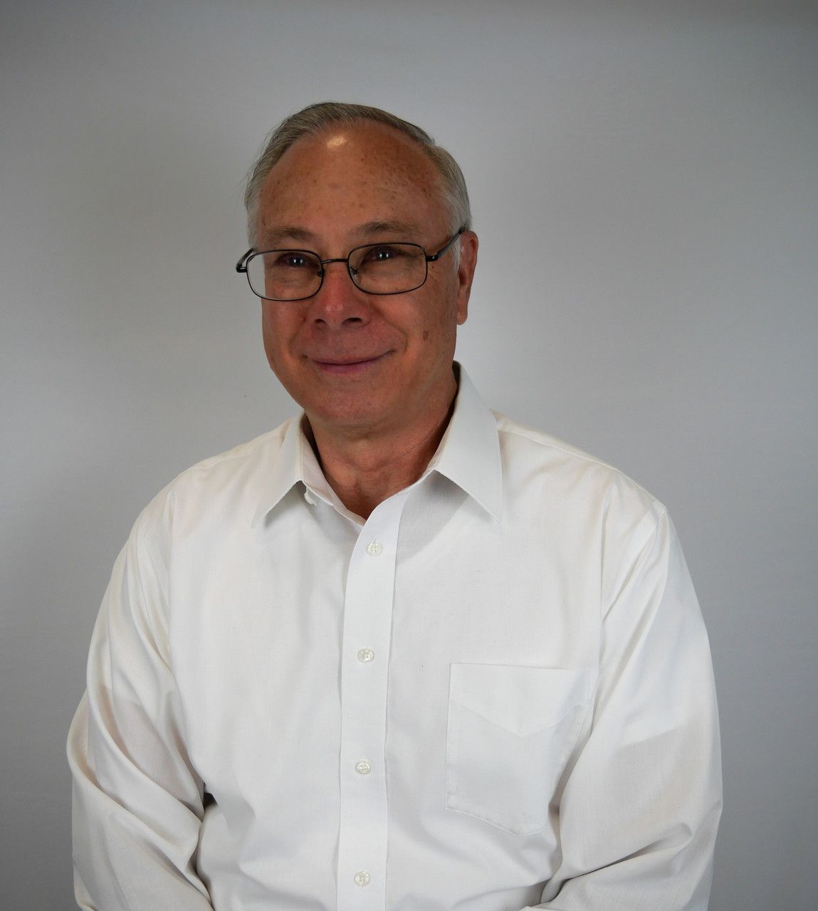 A man wearing glasses and a white shirt smiles for the camera