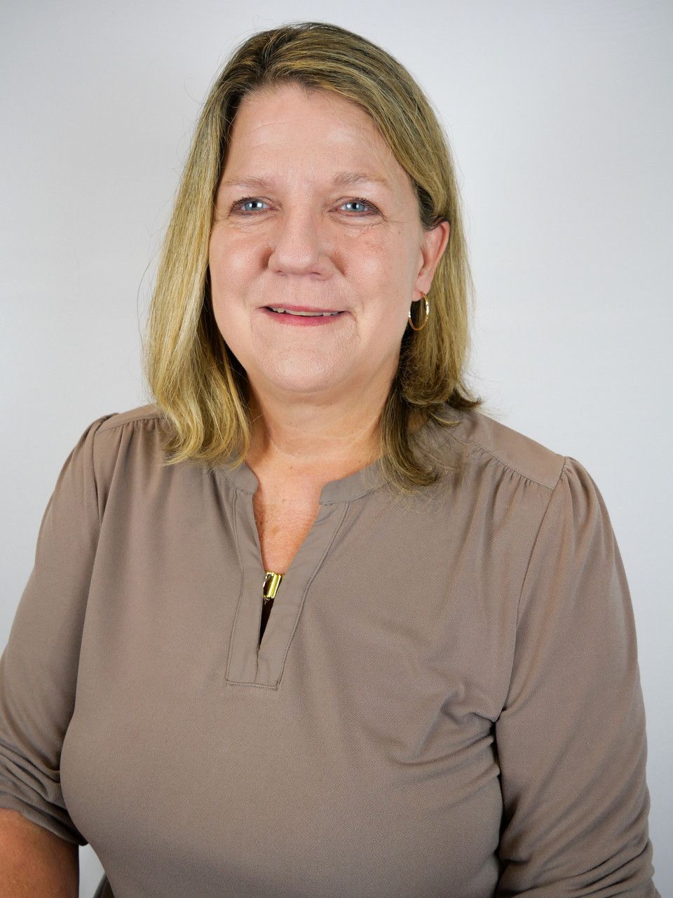 A woman in a brown shirt is smiling for the camera.