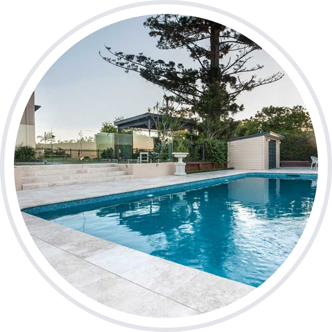 Swimming pool with blue water, surrounded by light-colored tiles. Shed and large tree in background.