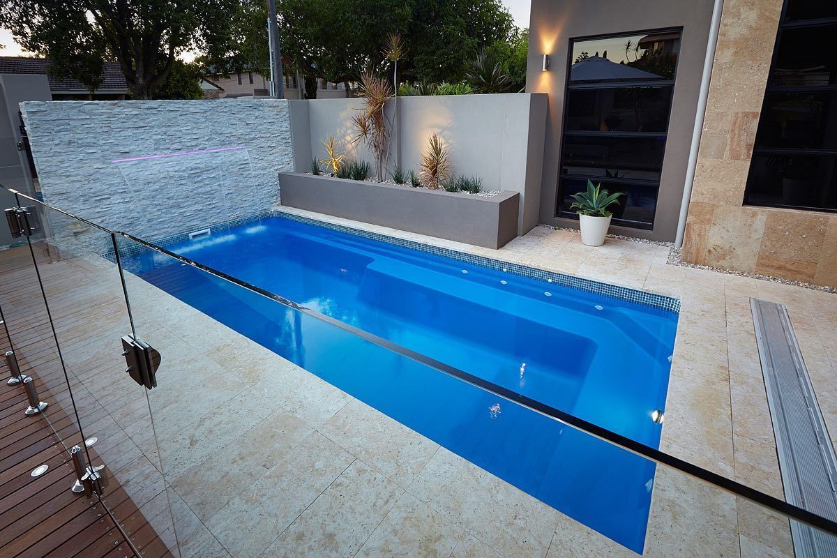 A small, rectangular swimming pool with blue water, surrounded by a patio and a glass fence.