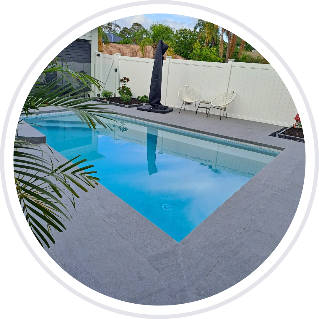 Rectangular pool with blue water, grey stone surround, white fence, and chairs.