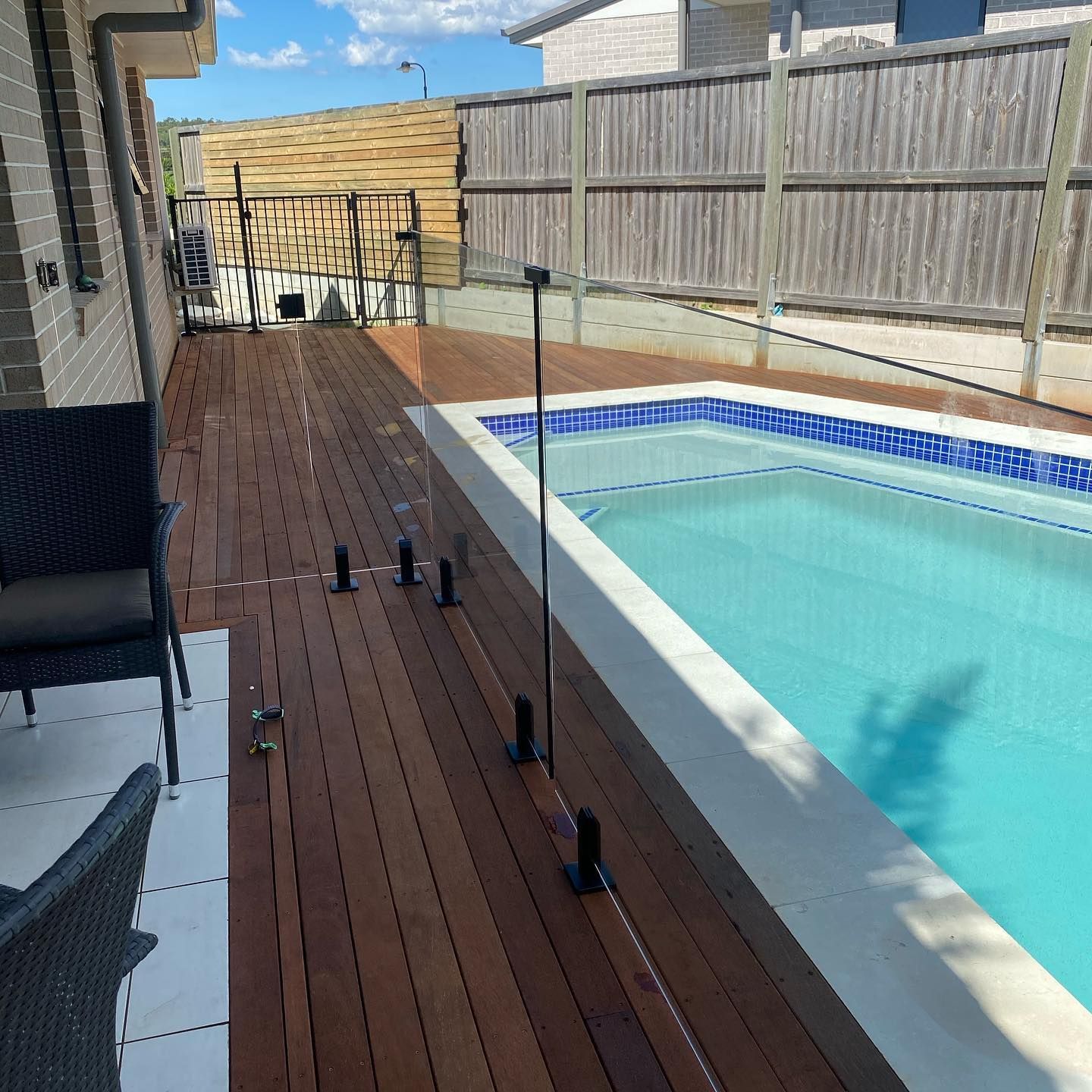 Pool with glass fence on a wooden deck; backyard setting.