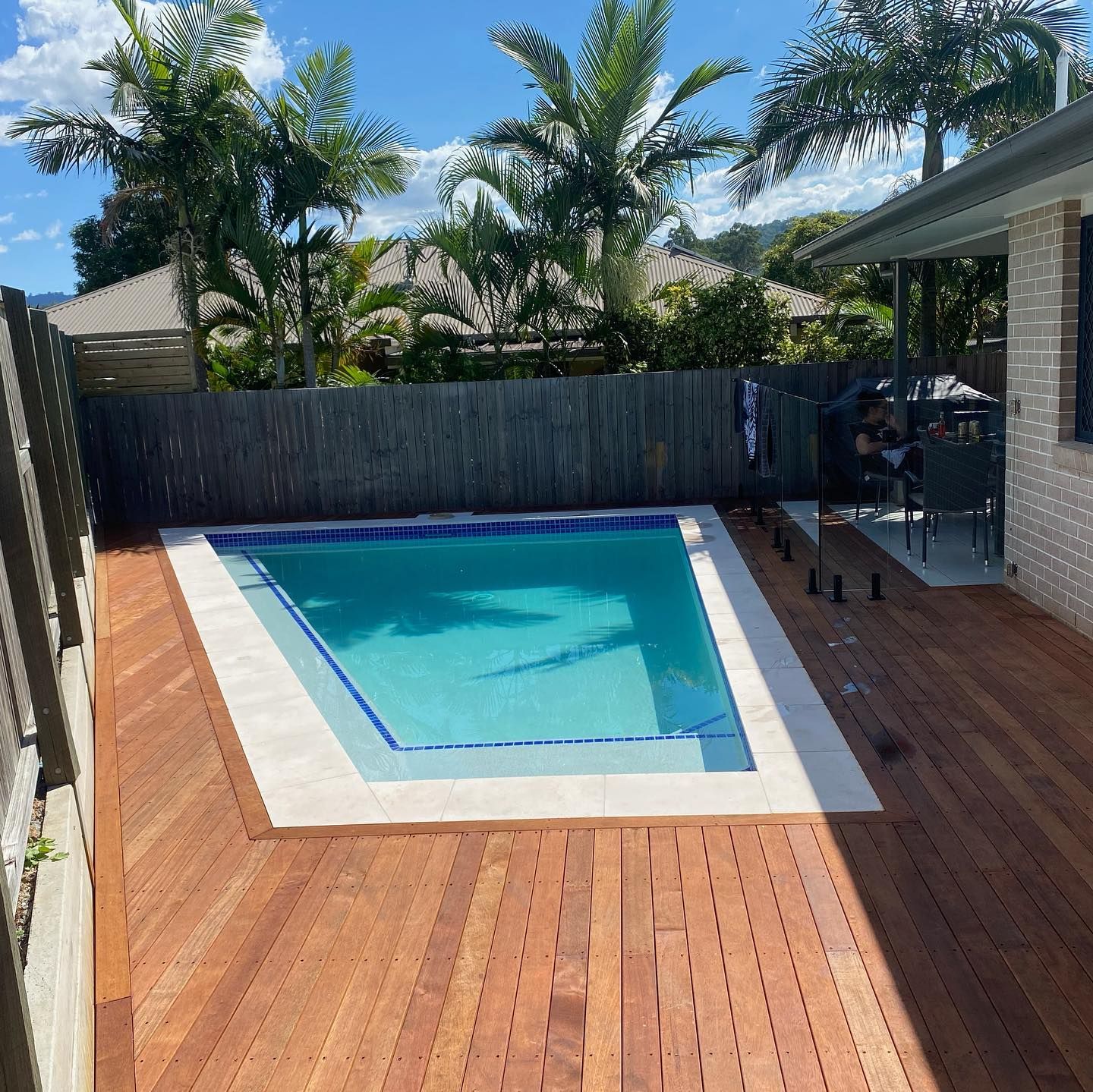 Backyard with a small swimming pool, surrounded by a wooden deck and a fence, sunny day.