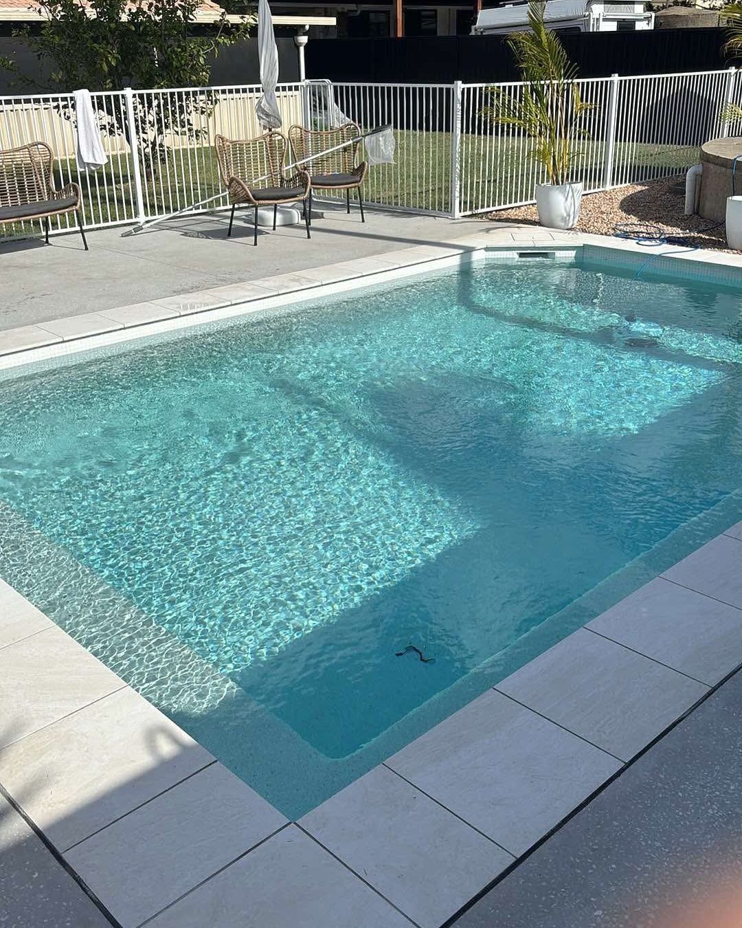 A clear, rectangular pool with turquoise water. White tile border, white fence in background.