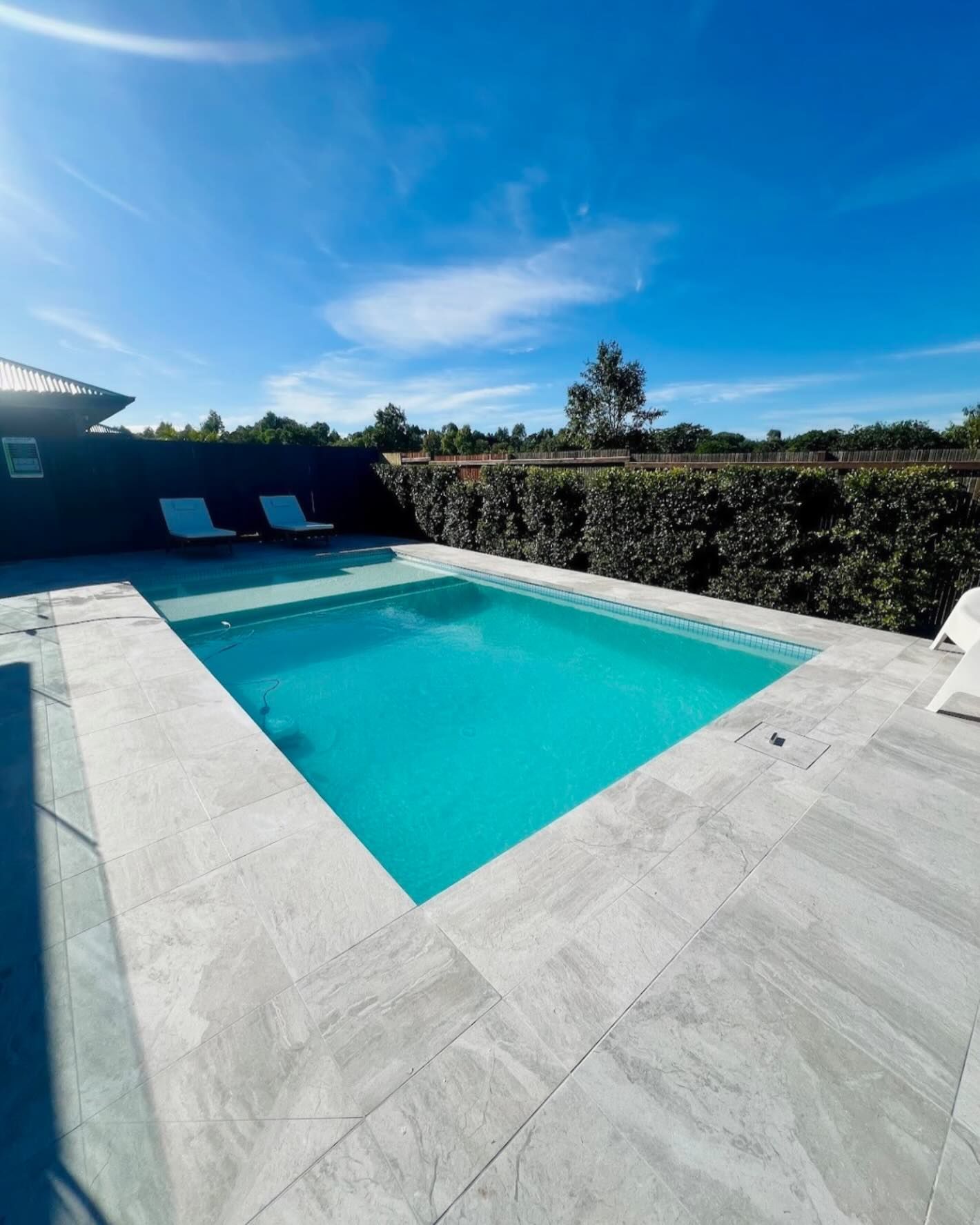 A rectangular pool with clear turquoise water, surrounded by stone patio, under a blue sky.