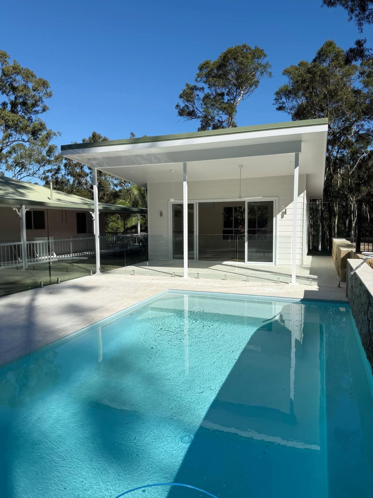White house with pool, trees. Bright blue sky. Sunny day.