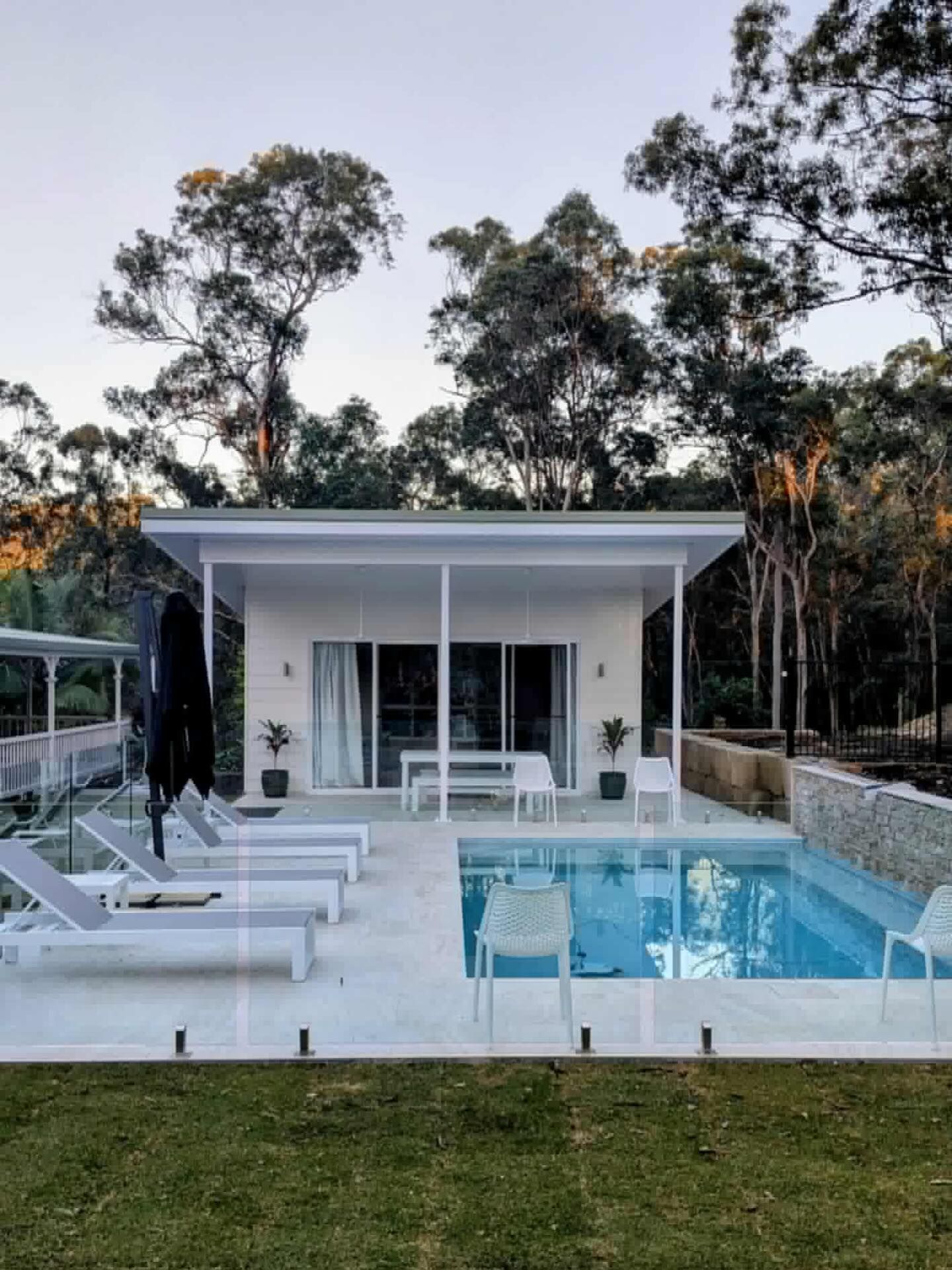 White modern home with a pool, lounge chairs, and trees.