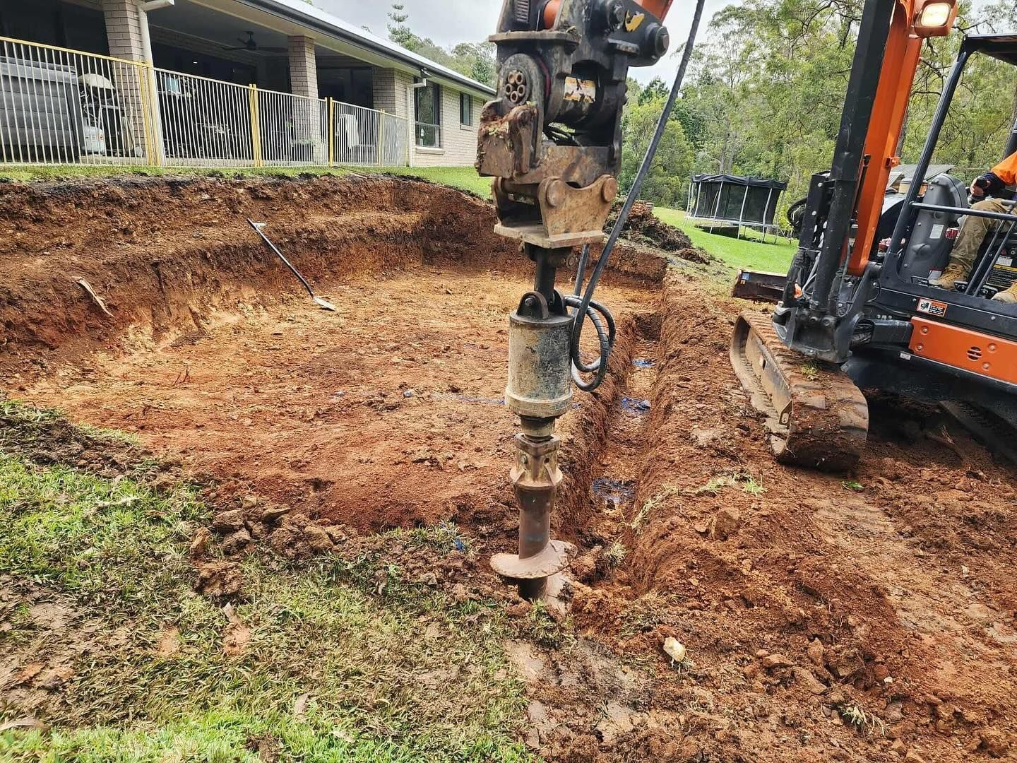 An excavator drilling into the earth in a grassy area near a building with zebra-striped bars.