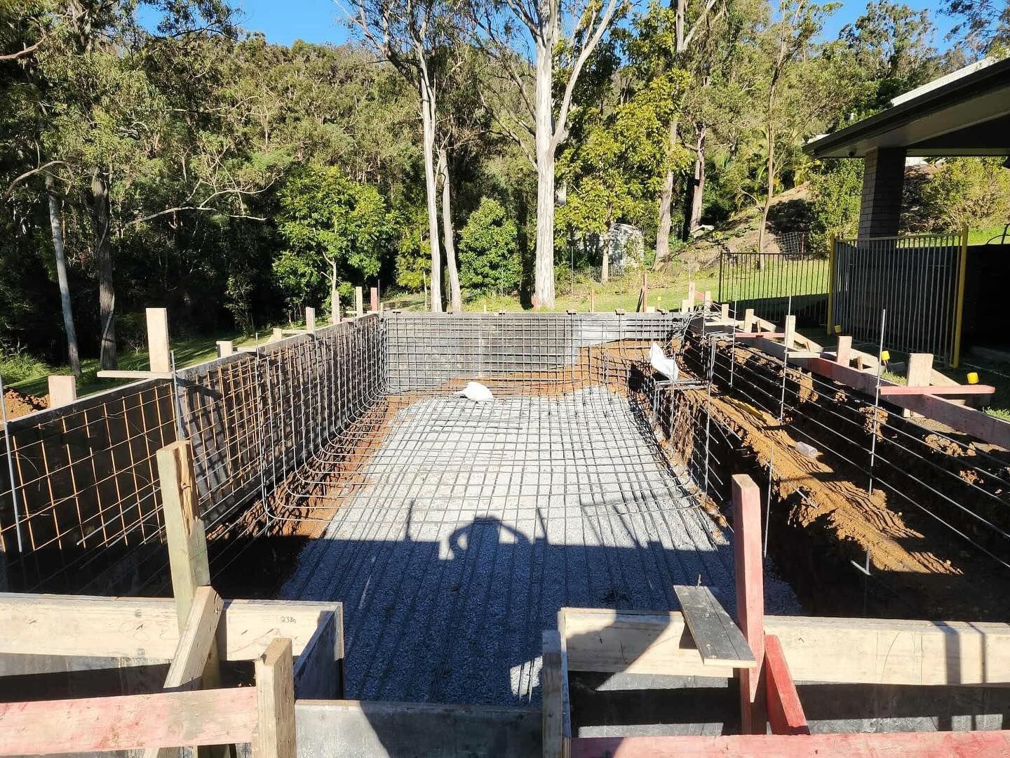 Construction of a rectangular pool; rebar framework set in an excavated area, surrounded by wooden forms.