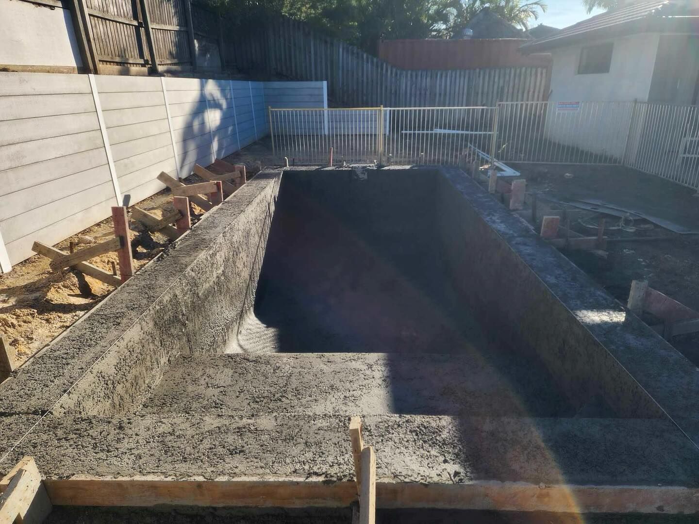 Concrete pool construction in backyard setting. Forms and framework visible.