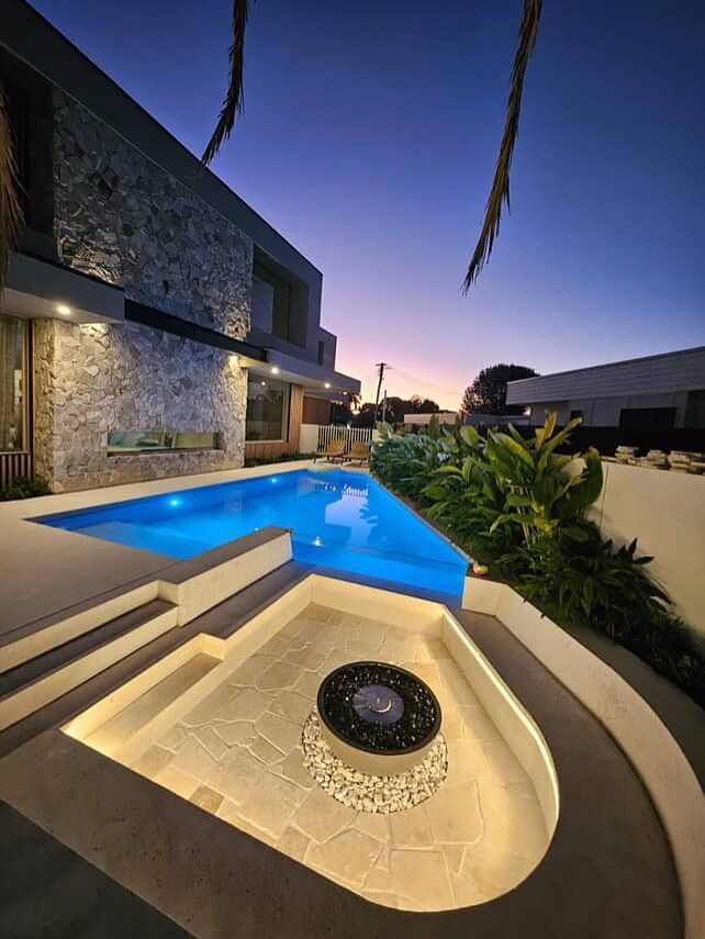 Modern home with a pool and fire pit lit at dusk.