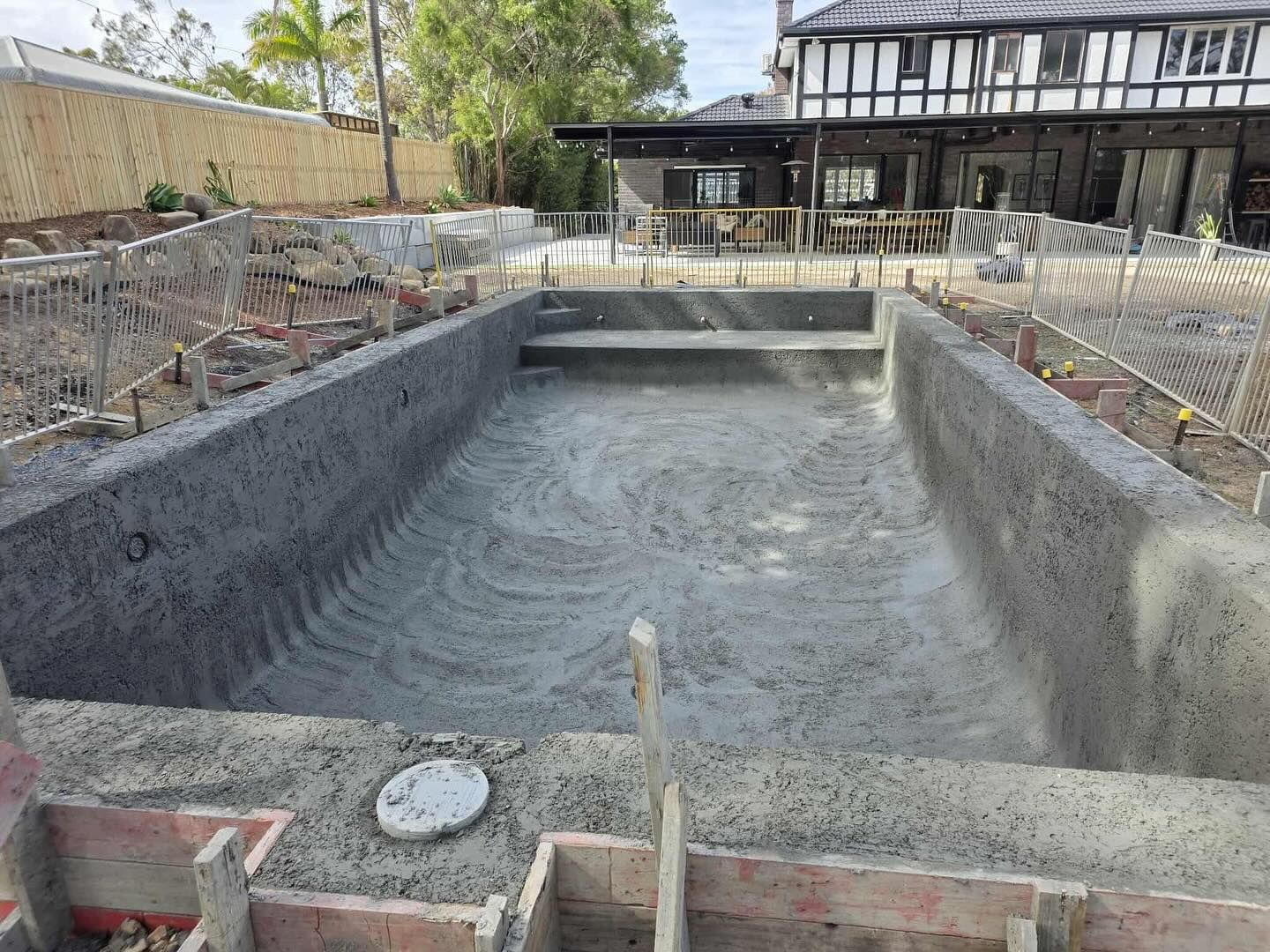 Newly built concrete swimming pool, surrounded by construction materials, in a residential backyard.
