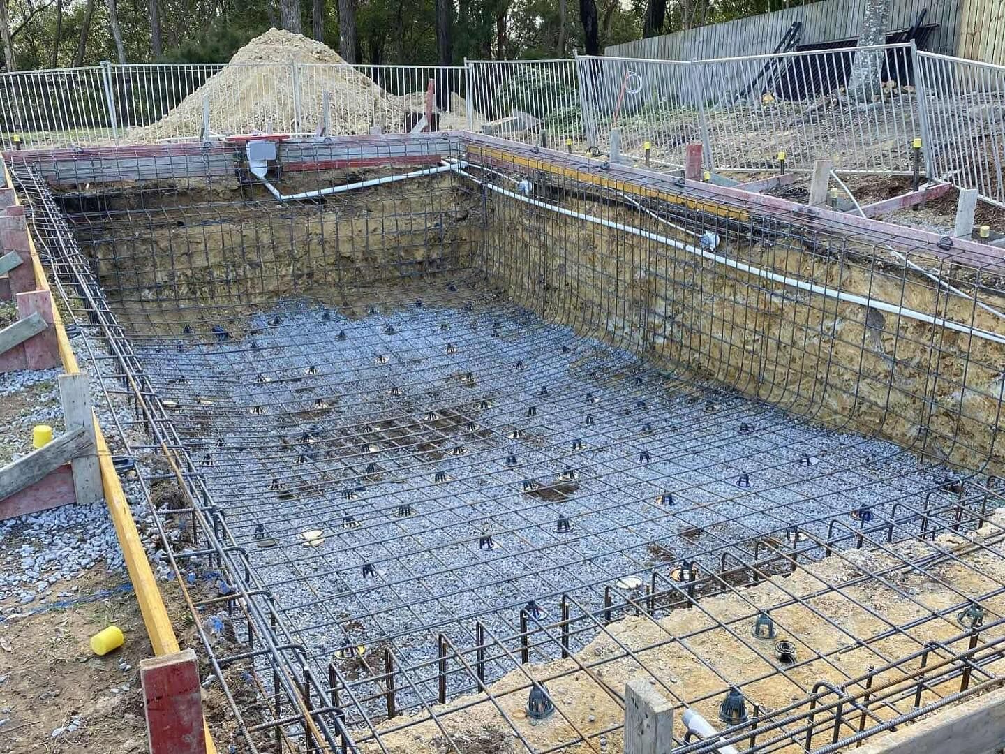 Pool under construction; rebar framework, gravel base, and brick retaining walls.