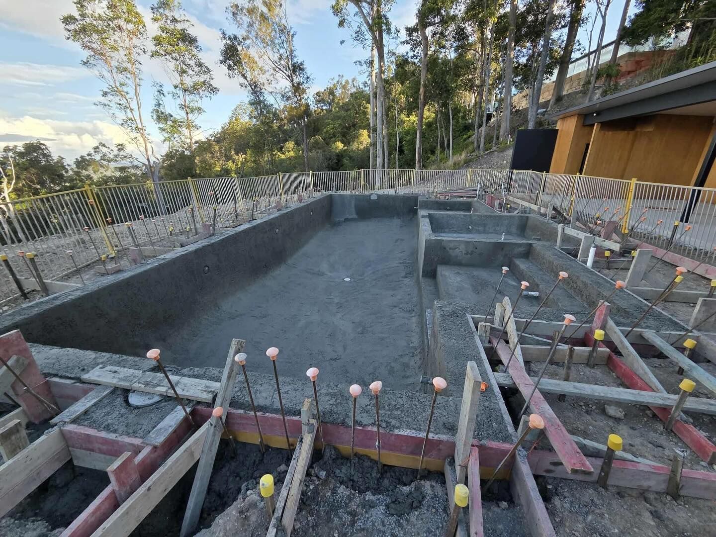Pool under construction, gray concrete, wooden forms, surrounded by trees and hillside.