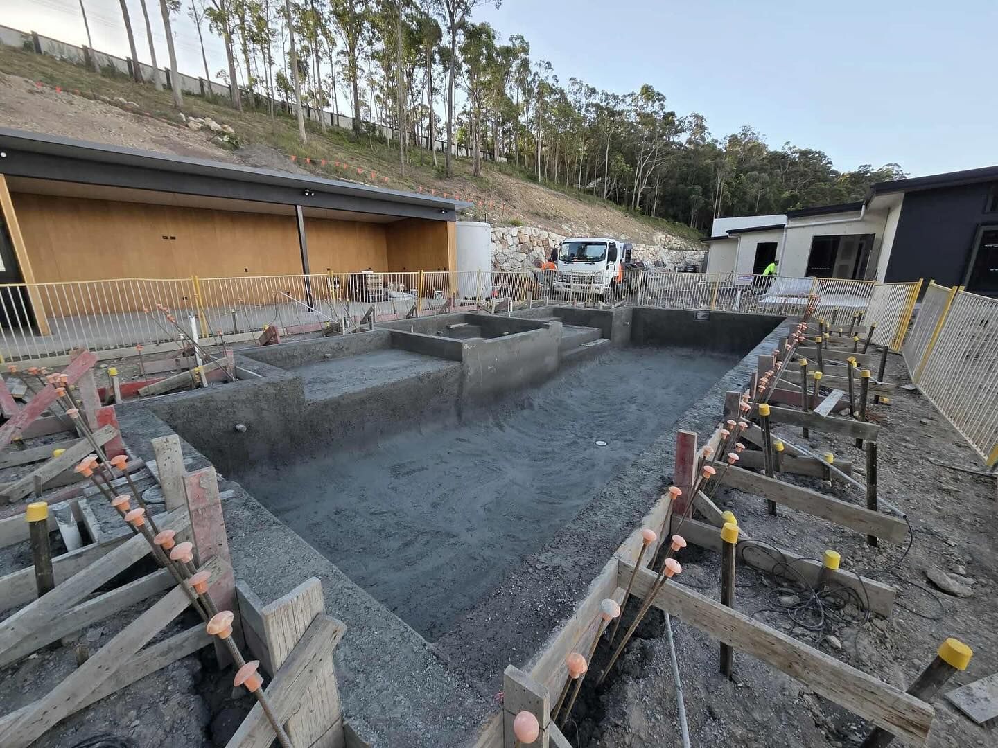 Construction site with a concrete pool under development, surrounded by wooden forms and a small truck.