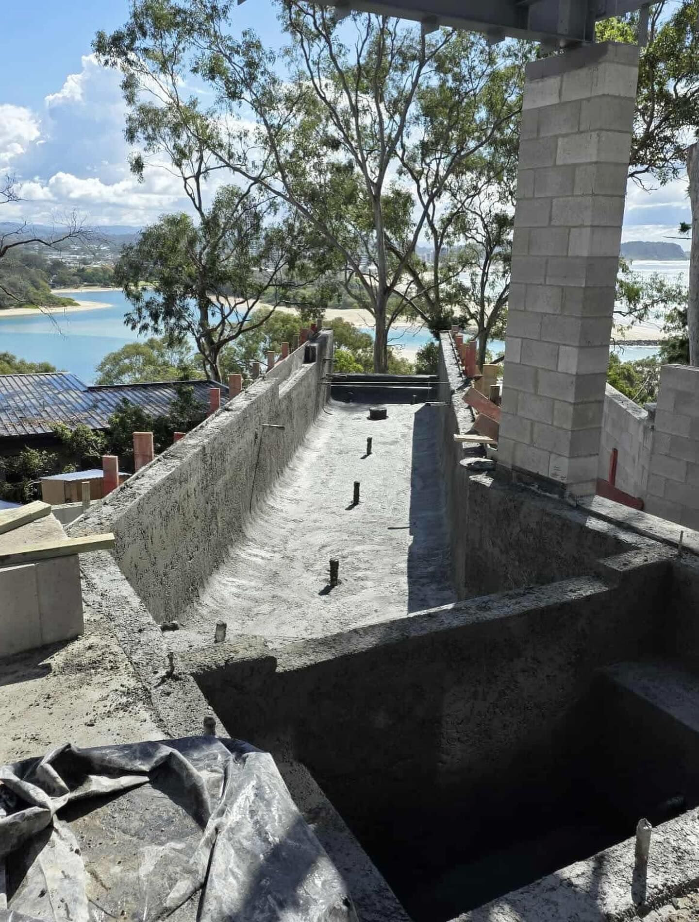 Construction site with concrete structures, view of water and trees.