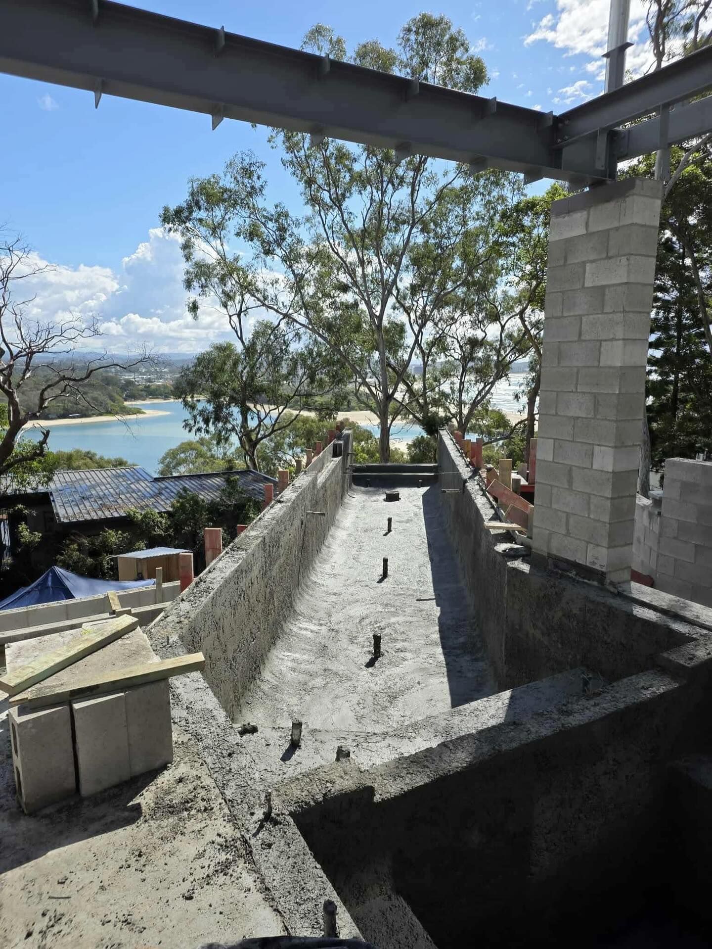 Construction site: concrete trough, cinder block walls, steel beam, overlooking a body of water.